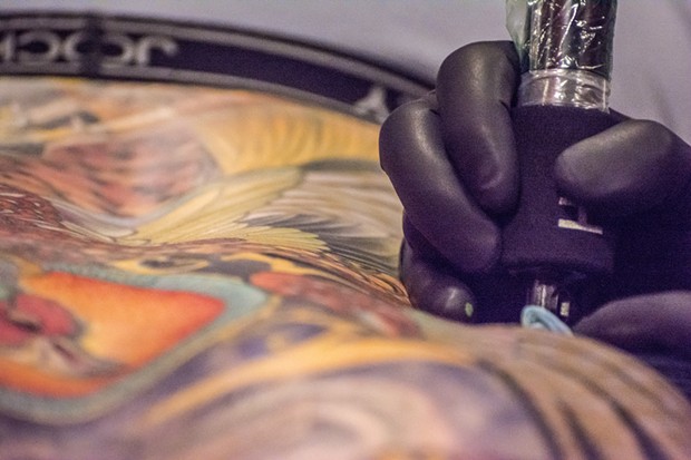 A close-up view reveals the artist's tattoo gun at work on the the "canvas" of a person's back. - MARK LARSON