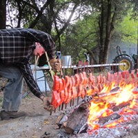 Frank Lake positions stakes with Chinook salmon fillets around a hot bed of madrone coals in a small grove between the MKWC building and the Klamath River.