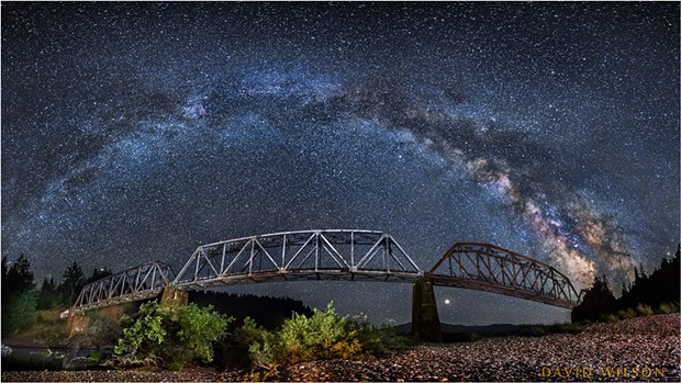 The Milky Way arcs from horizon to horizon above the South Fork Bridge in this panorama on the Main Fork Eel River, Humboldt County, California. July, 2018. - DAVID WILSON