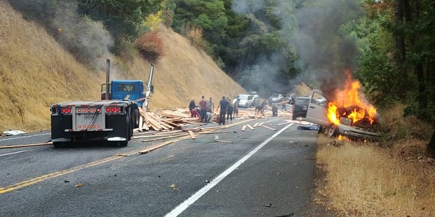A vehicle burns as onlookers attempt to remove lumber from the road. - PHOTO COURTESY OF  CHRIS BRANNAN