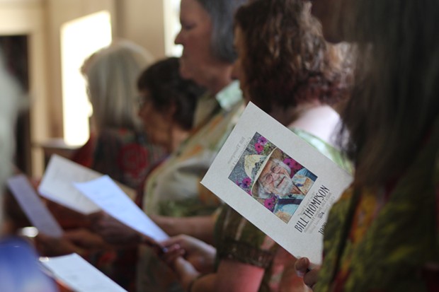 A member of the Threshold Choir opens up Thompson's memorial program where lyrics to the song "Walking Each Other Home," is printed. The group and attendees ended the memorial service arm in arm while singing this song together. - PHOTO BY NATALYA ESTRADA