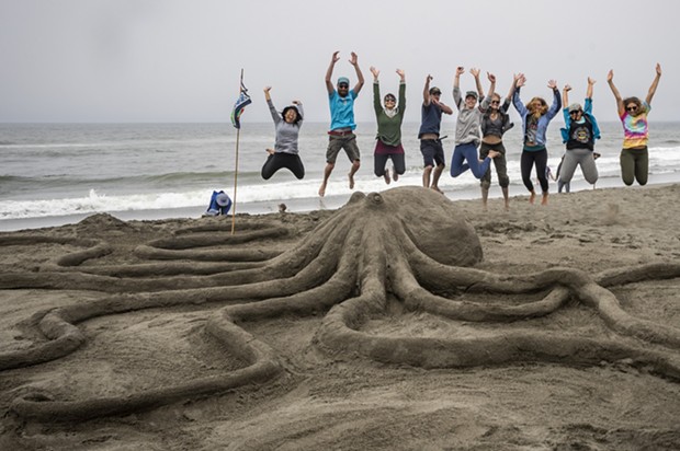 The Northcoast Environmental Center team members took to the air when they finished their "Lend a Hand, or Eight" sand sculpture. It later won the People's Choice award. - PHOTO BY MARK LARSON