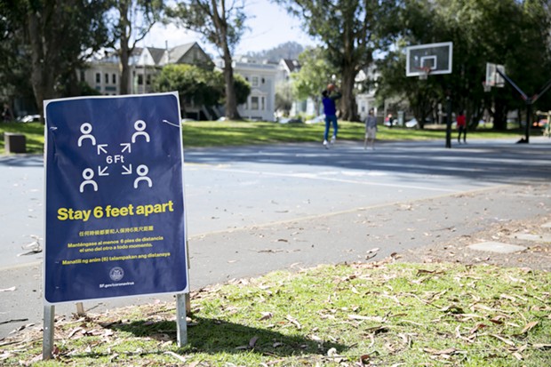 People play basketball at a San Francisco park behind a sign reminders park-goers to maintain social distancing on March 25, 2020. - ANNE WERNIKOFF FOR CALMATTERS