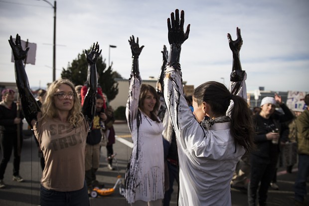Leslie Castellano (right)  leads three other protesters letting  molasses flow down their arms in protest of Wells Fargo's investments in the DAPL. - SAM ARMANINO