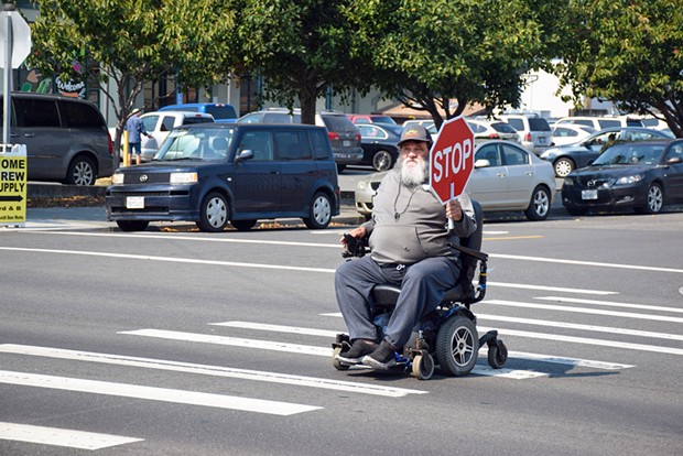 Robert Lane crosses Fourth Street using a hand-held stop sign loaned to him by Tri-County Independent Living, which has reached out to officials to express concern about pedestrian safety in the area.