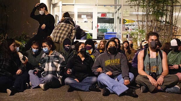 Protesters sit outside the barricaded entrance of Siemens Hall, interlocking arms, on April 22, in an effort to prevent officers from attempting to enter the building.