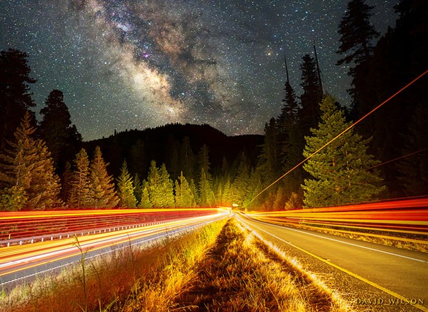 A view beside the on-ramp to southbound U.S. Highway 101 from Vista Point. The Milky Way converges in the distance with the streaking taillights of semi trucks passing by on the left and right. Just around the distant corner is the entrance to the north end of the Avenue of the Giants. All the light of the landscape was provided, like paint strokes, by the passing trucks. June 30, 2024.