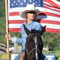 A Native woman carries the flag during the Hoopa Rodeo.