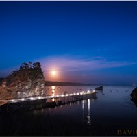 The full moon rises over Little Head, Trinidad Pier, and Trinidad Harbor. Trinidad Head is the silhouetted land mass on the right.