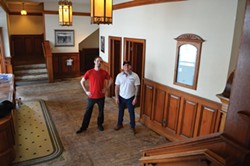 PHOTO BY GRANT SCOTT-GOFORTH - McKinlay and Neff stand in the Minor’s lobby, stripped of carpeting and concessions equipment. Many of the lobby’s fixtures, including the grandfather clock and opening night photo, remain.
