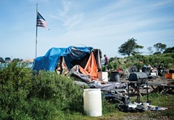 PHOTO BY MARK MCKENNA - A tattered American flag flies over a soon-to-be razed camp in the PalCo Marsh on May 1.