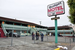 PHOTO BY THADEUS GREENSON - With the tenants having moved on, city officials watch as the last of the Budget Motel's windows and doors are boarded up.